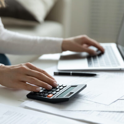 Close up young woman using calculator and laptop, checking domestic bills, sitting at table with financial documents, managing planning budget, accounting expenses, browsing internet service